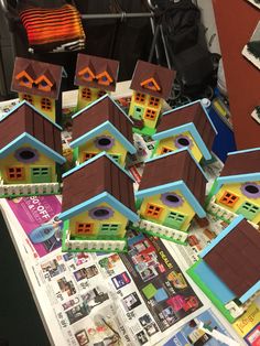 many small birdhouses are sitting on top of a table with papers and magazines around them