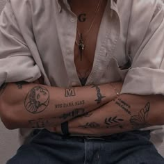 a man with tattoos on his arms and chest is sitting in front of a white wall