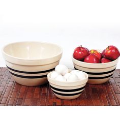 three bowls with apples in them sitting on a wooden table next to an egg holder