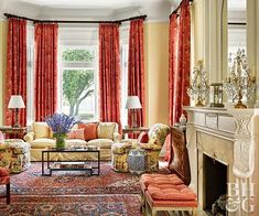 a living room filled with furniture and a fire place in front of a window covered in red curtains