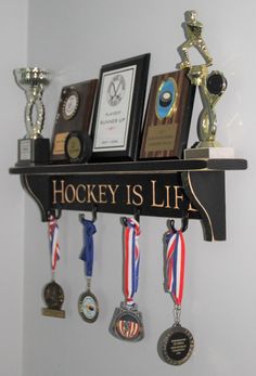 there are medals hanging on the shelf with plaques and trophies around it that says hockey is life