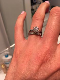 a woman's hand with two wedding rings on top of her finger, in front of a mirror