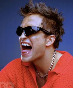 a man with sunglasses and a chain around his neck is making a funny face while wearing an orange shirt