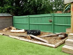 a green fenced in back yard with wooden logs and rocks on the ground next to it