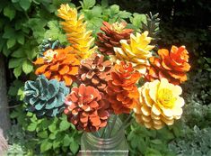 a vase filled with lots of colorful flowers in front of green leaves and shrubbery