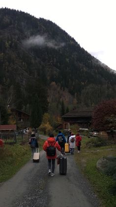 several people walking down a dirt road carrying suitcases and bags in front of a mountain