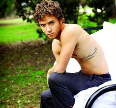 a shirtless young man sitting on top of a white car with his hand in his pocket