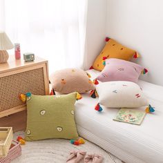 four pillows on a bed with colorful pom - poms around them and a radio in the corner