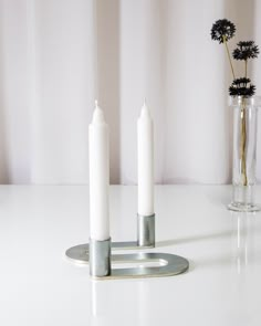 three white candles sitting on top of a table next to a vase with flowers in it