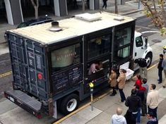 a food truck is parked on the side of the road with people standing around it