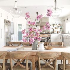 a kitchen table with chairs and a vase filled with pink flowers on top of it