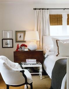 a bedroom with white bedding and two chairs in front of the bed, along with pictures on the wall