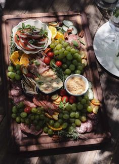 a wooden platter filled with meat, cheese and fruit on top of a table