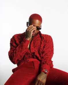 a man in red is sitting down with his hands on his face and wearing sunglasses