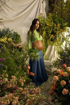 a pregnant woman standing in a garden surrounded by flowers and greenery with her belly exposed