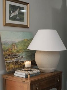 a white lamp sitting on top of a wooden table next to a painting and a candle