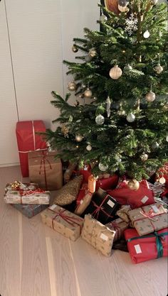 a christmas tree with presents under it on the floor next to a pile of wrapped gifts