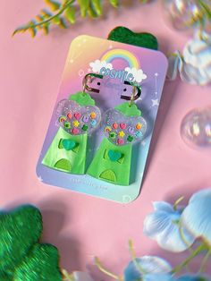 two little green teddy bears are in the shape of keychains on a pink background