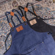 two denim aprons sitting on top of a rug with leather tags attached to them