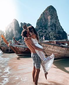 a man and woman kissing on the beach with boats in the water behind them at low tide