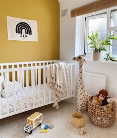 a baby's room with yellow walls and white crib, stuffed giraffe toy