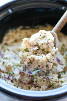 a spoon full of mashed potatoes in a crock pot with parsley on top