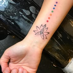 a person's hand with a small tattoo on the wrist and colorful dots around it