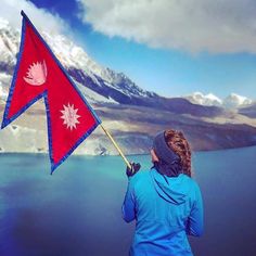 a woman holding a red and blue flag in front of a mountain range with snow on it