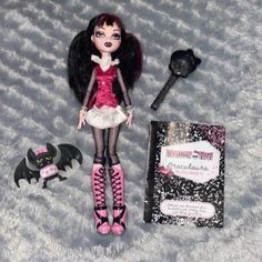 a doll with black hair and pink dress next to a book, batwing wand