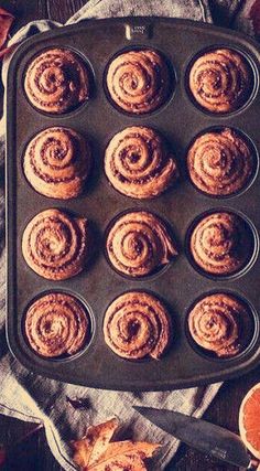 a muffin pan filled with cinnamon rolls next to an orange and some other food