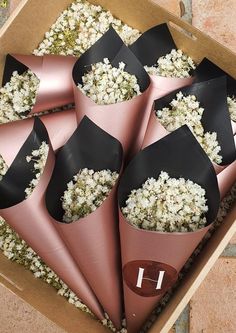 six pink cones with black bows are in a cardboard box filled with white and brown flowers