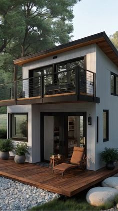 a small house with a deck and chairs on the front porch, surrounded by rocks