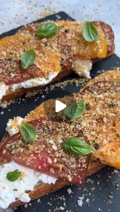 two pieces of bread with cheese, tomato and basil on them sitting on a black plate