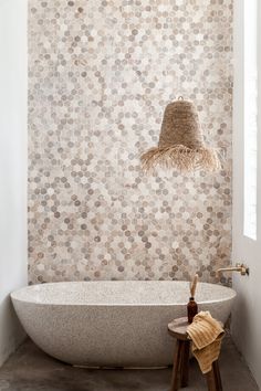 a white bath tub sitting under a window next to a wooden stool and wall mounted light