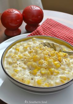 a bowl of corn and cheese soup on a white plate with two red tomatoes in the background