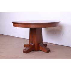 a round wooden table sitting on top of a floor next to a white brick wall