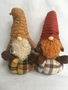 two stuffed gnomes sitting next to each other on a white surface with one wearing a red hat