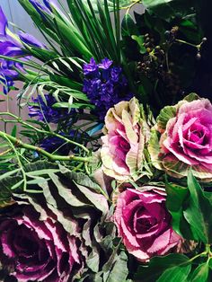 a bouquet of flowers with green leaves and purple flowers in the center, sitting on a table