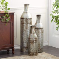 three metal vases sitting next to each other on a rug in front of a wooden cabinet