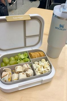 an open lunch box with grapes, crackers and other food in it on a table