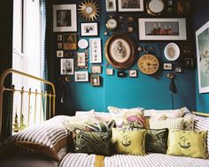 a bed with lots of pillows and pictures on the wall next to it in front of a window