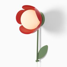 a red flower with green stems on a white wall next to a small light bulb