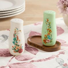 two ceramic vases sitting on top of a wooden tray next to plates and flowers