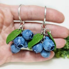 small blueberries with green leaves are hanging from silver earwires on a hand