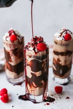 two glasses filled with ice cream and raspberries on top of a white table