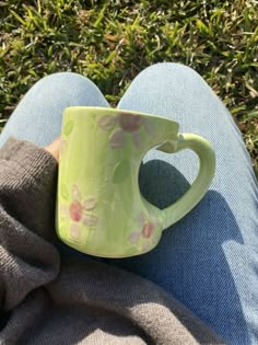 a green coffee cup sitting on top of someone's lap in the grass with their legs crossed