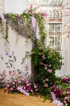 an arrangement of flowers and greenery in front of a window