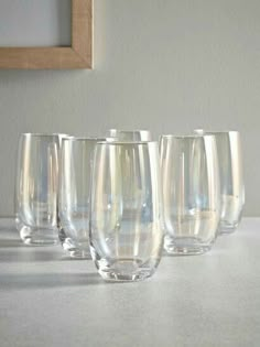 six clear wine glasses lined up on a white countertop next to a framed photograph