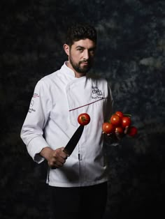 a man holding tomatoes and a knife in one hand while wearing a chef's coat