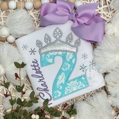 a birthday shirt with the number two on it and a purple bow is laying next to some ornaments